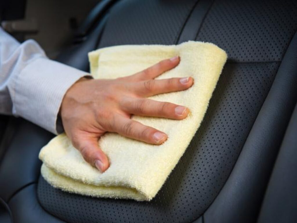 A person wiping the seat of a car with a towel