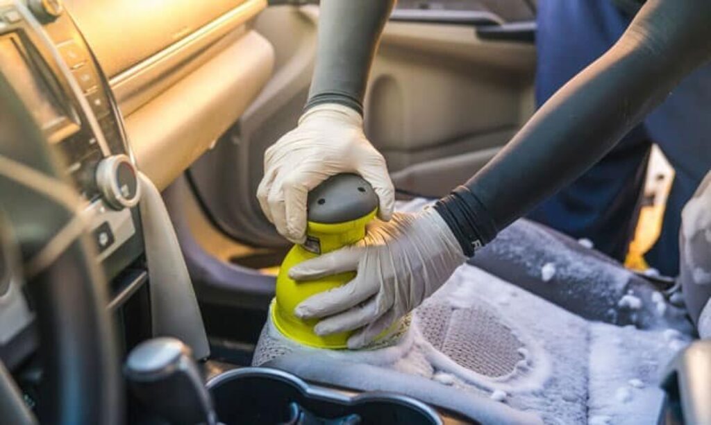 A person is cleaning the seat of a car using a shampoo applying tool